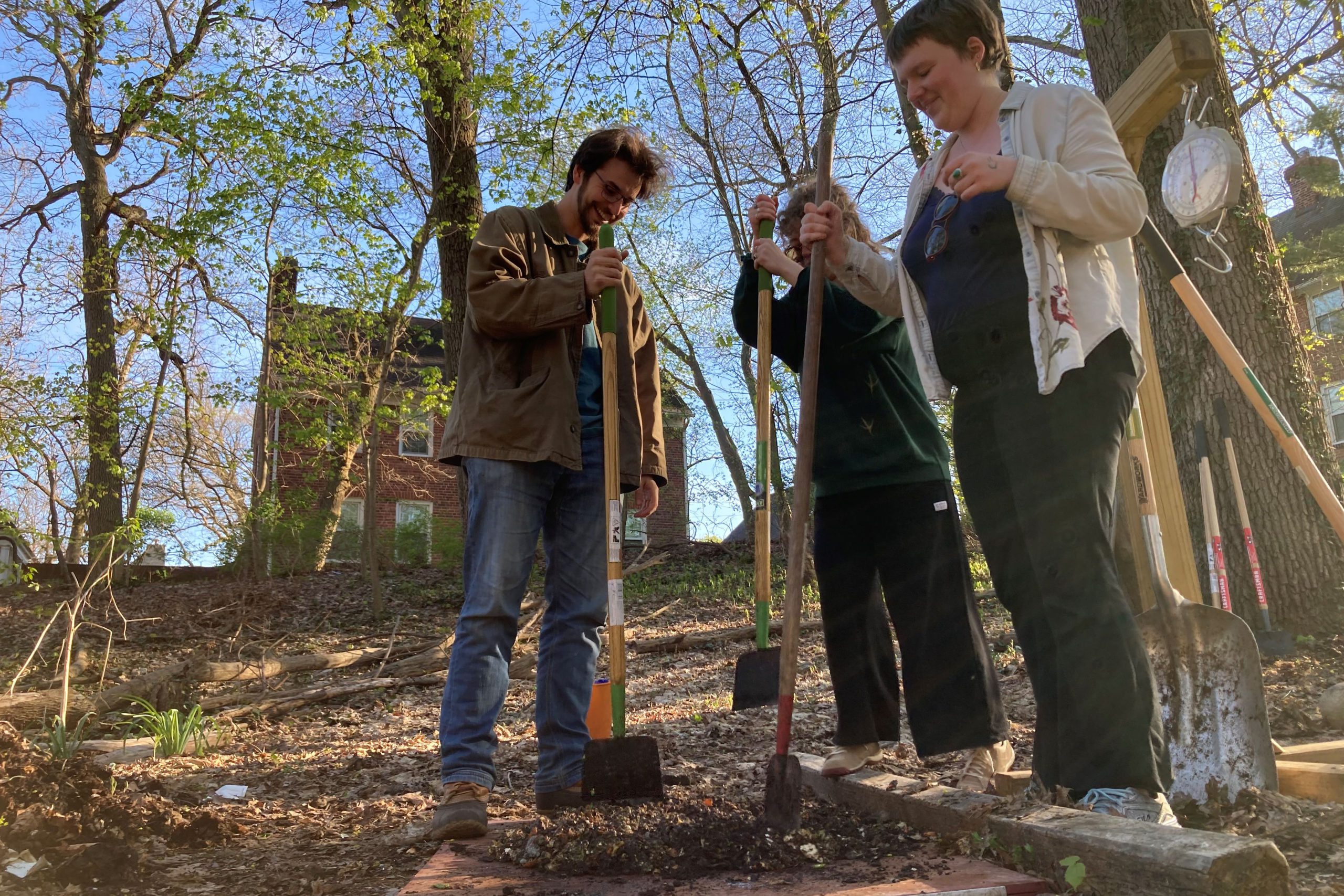 Three students standing in the woods with yard tools